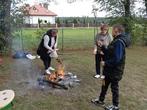 15. Zdjęcie przedstawia trzy osoby, które pieką kiełbaski i chleb nad ogniskiem